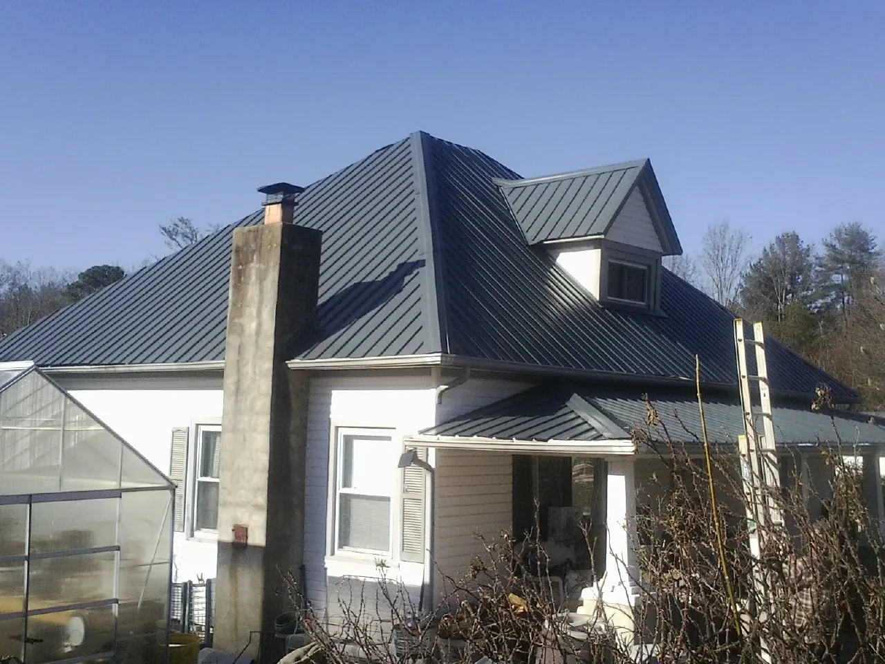 Dark blue standing seam metal roof on a white farmhouse with dormer — Slate & Tile Roof Repair by Roofing Brothers in Axtell