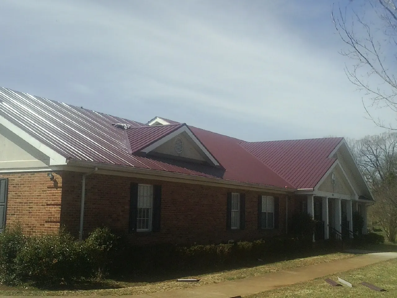 Red metal roof with gabled entries on a long brick building, from a Hail Damage Roof Repair job in Axtell