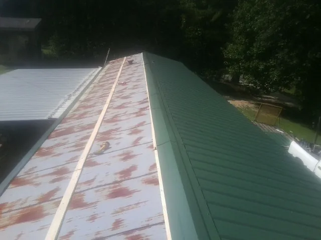 Old rusted panels beside newly installed green metal roofing — Wind Damage Roof Repair by Roofing Brothers in Axtell