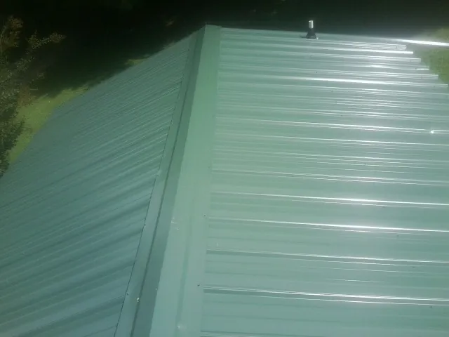 New green metal panels meeting at the ridge of a roof — Flat Roof Repair work by our crew in Axtell