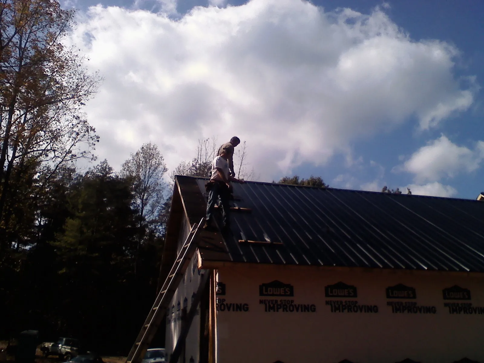 Roofer fastening dark metal panels high against a cloudy sky, from a Roof Inspection job in Axtell
