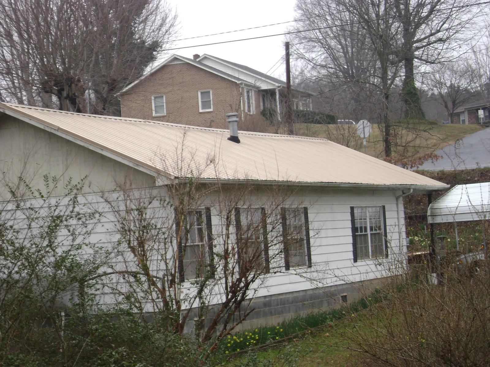 Tan metal roof on a white sided house set into a hillside — Commercial Roofing by Roofing Brothers in Axtell